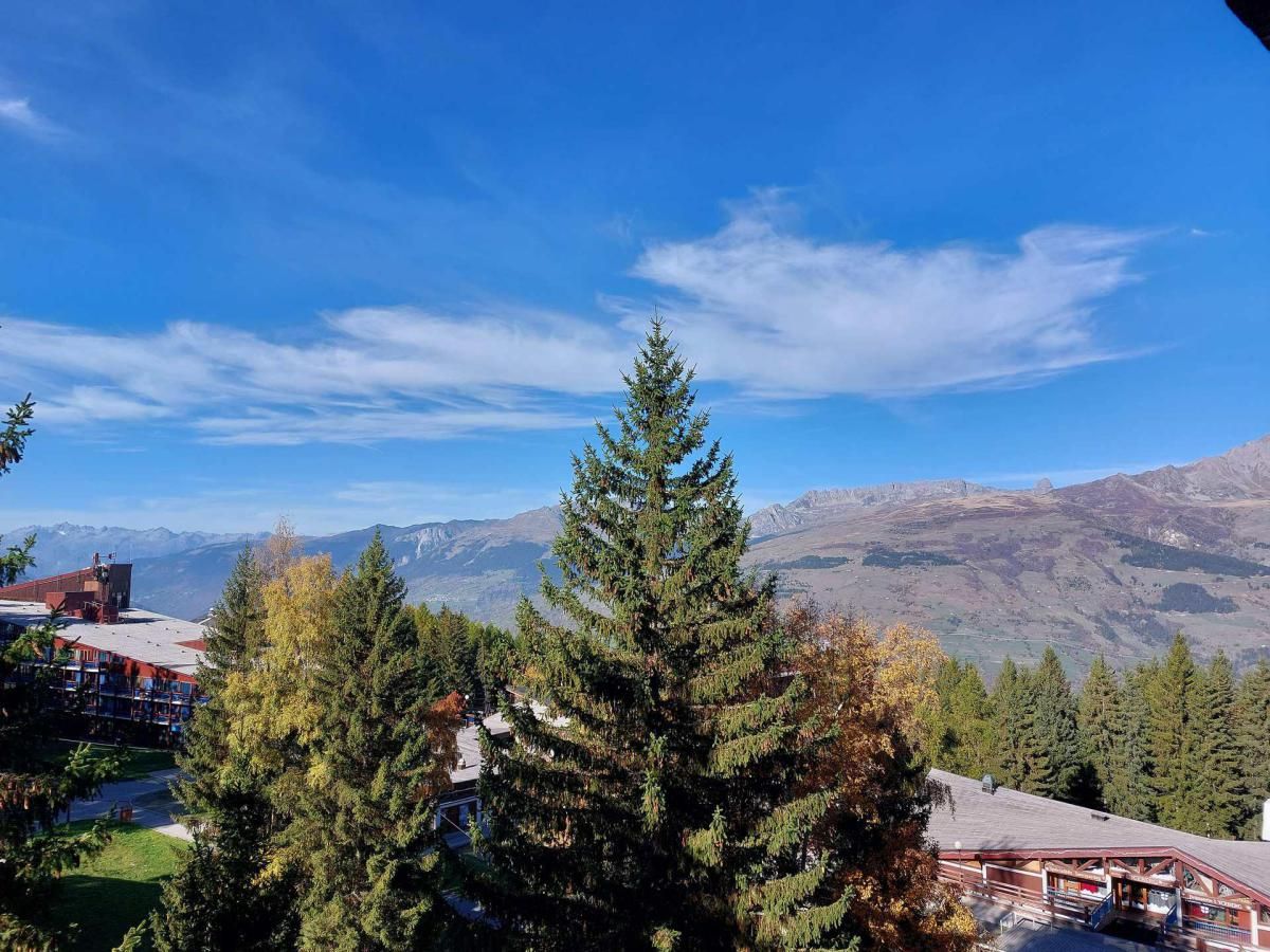 A mountainous landscape with a clear sky, a prominent evergreen tree, and a building with a red roof in the foreground.