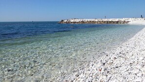 Una playa de guijarros con agua cristalina y un rompeolas rocoso.