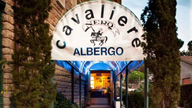 Entrada de un hotel con un letrero que dice "Cavaliere Albergo" y un corredor cubierto.