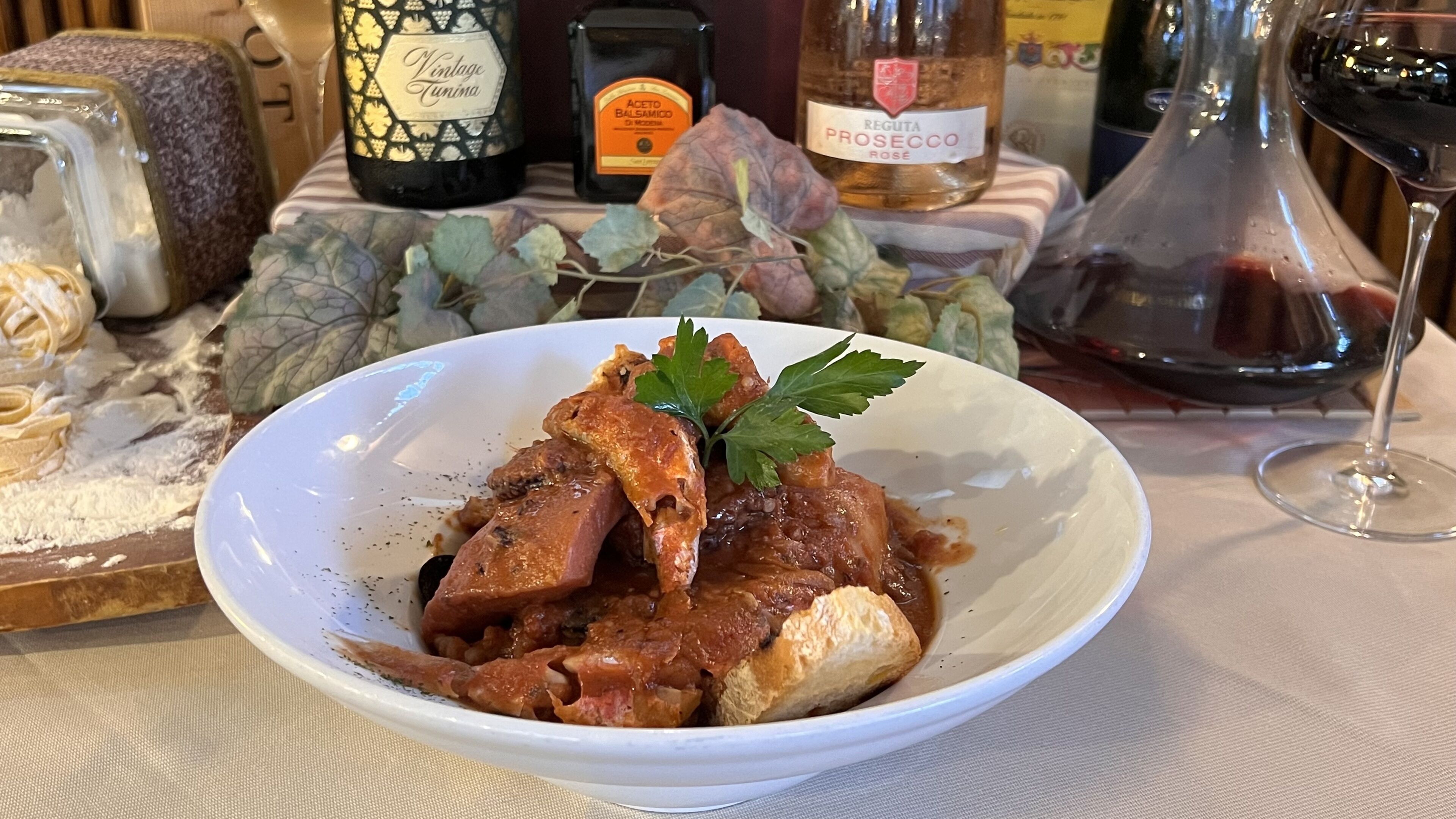 Eine Sch üssel mit Essen, ein Weinglas und Flaschen im Hintergrund.