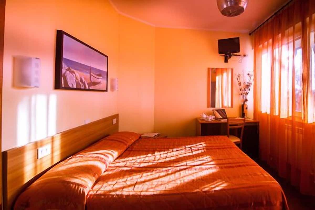 A hotel room with a bed, a desk, a chair, a television, and a window with curtains.