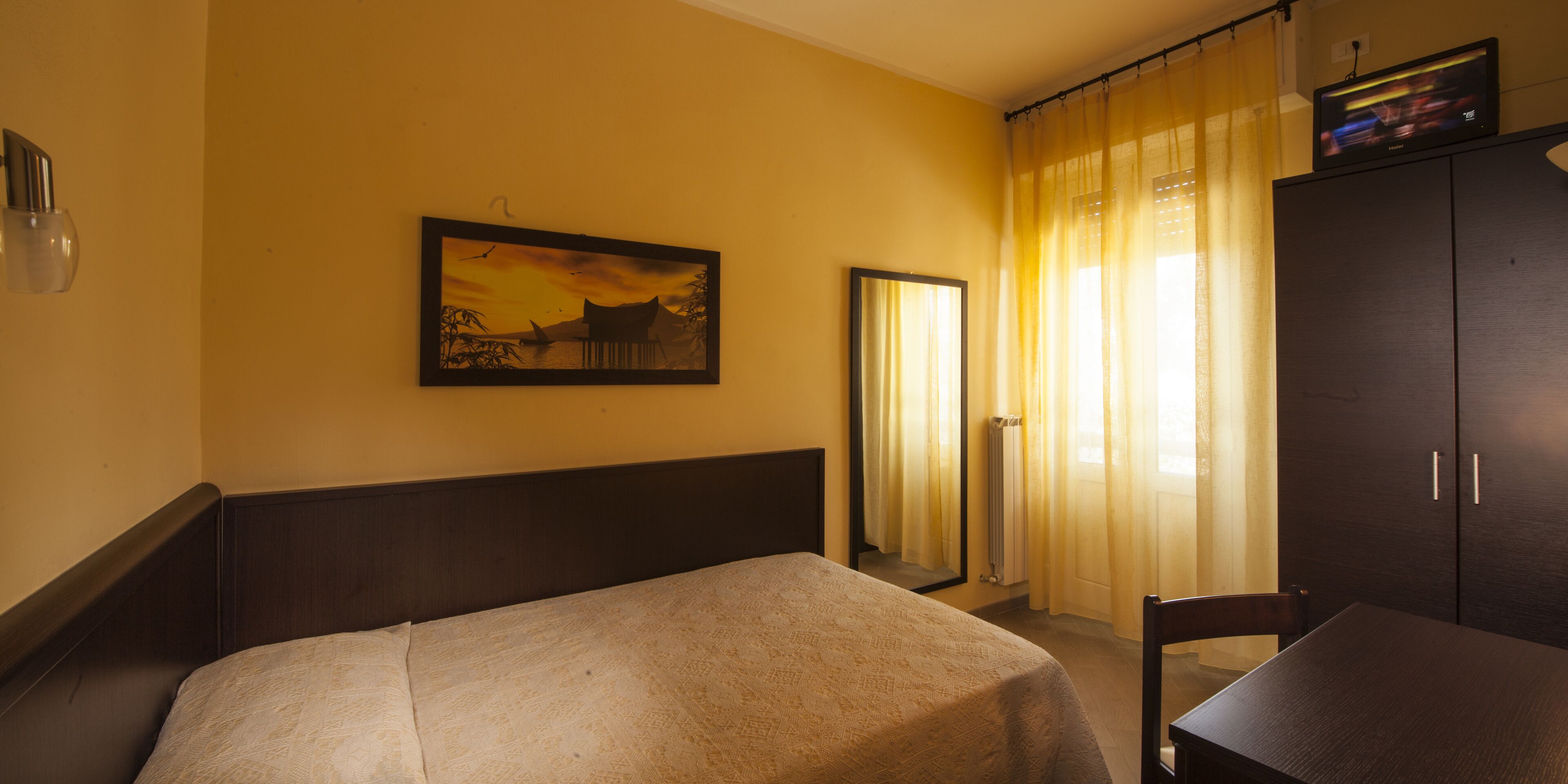 Habitación de hotel con cama, una silla, una mesa, un cuadro en la pared y un armario.