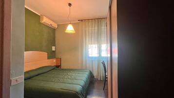 A room with a bed, an air conditioning unit, a lamp, and a window with curtains.