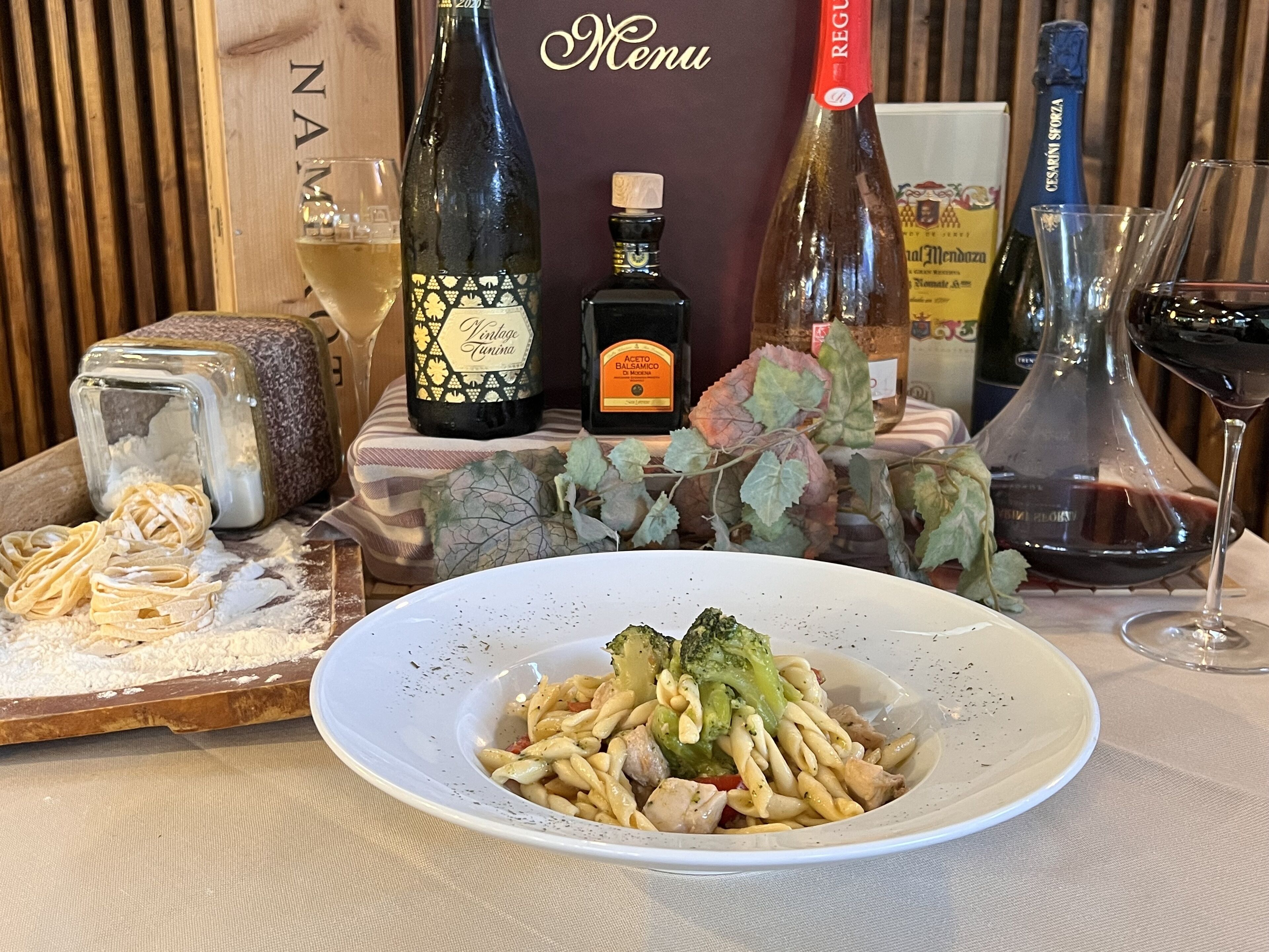 Ein Esstisch mit Pasta, Weinflaschen und einer Speisekarte.