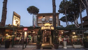 Un restaurante con terraza, un letrero de neón y plantas en macetas.