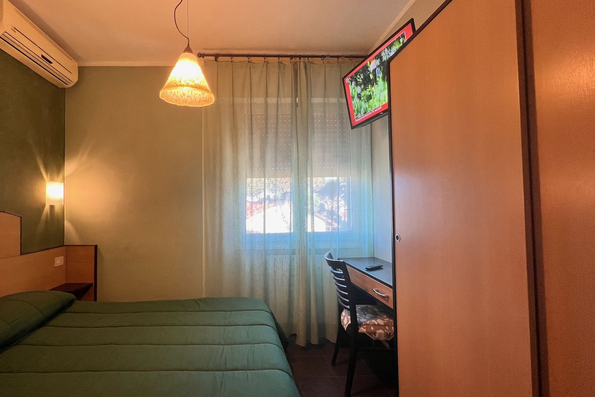 A room with a bed, a desk, a chair, a TV, and a window with curtains.