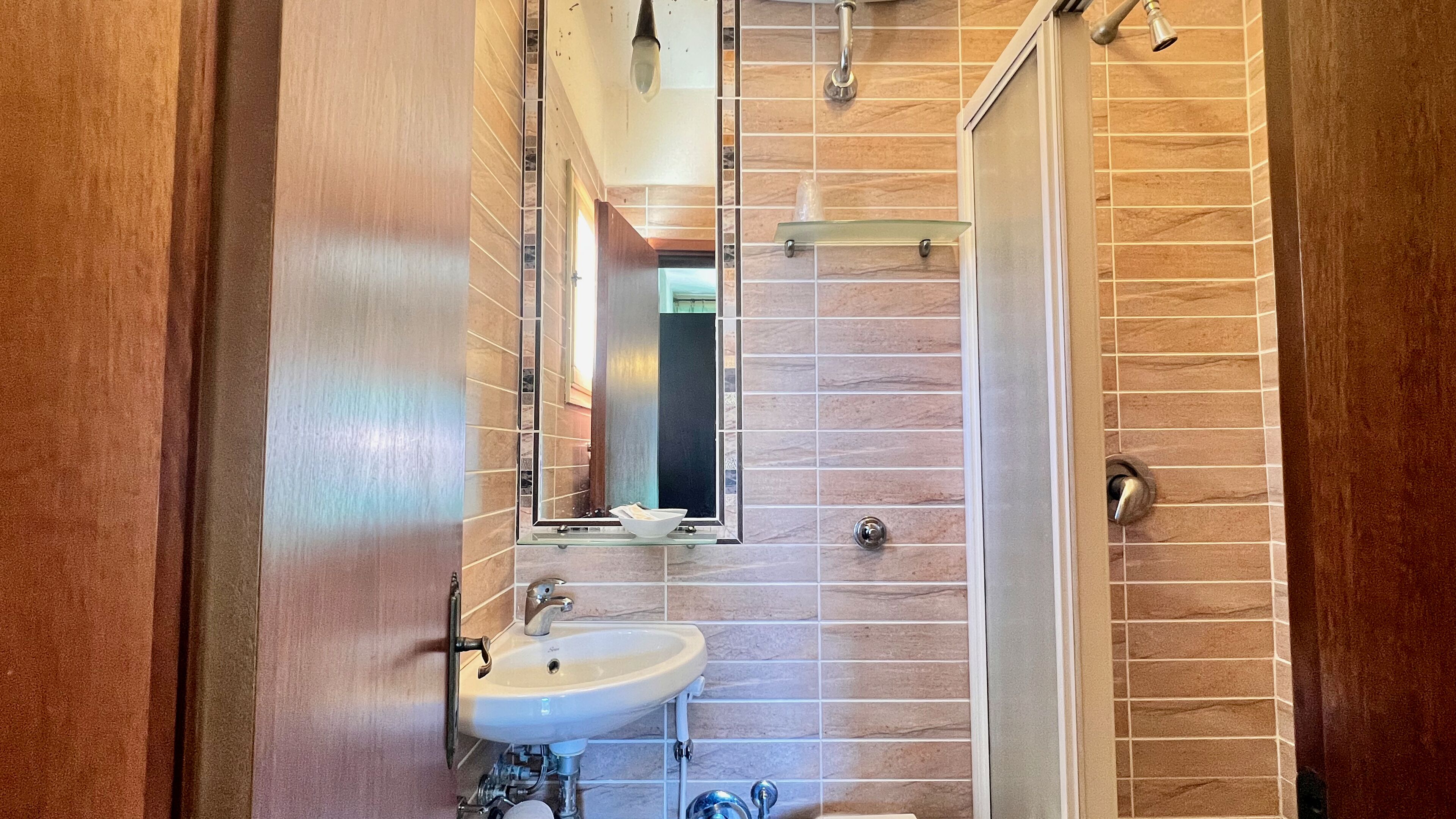 Ein Badezimmer mit einem Holzkosmetikschrank, einem Waschbecken, einem Spiegel und einer Duschkabine.