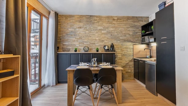 A modern kitchen with a wooden table and chairs, a brick accent wall, and built-in appliances. - 200m from ski slopes, 1st floor, view resort, swimming pool, balcony, tv, ski locker, 24m² (Les Orres)