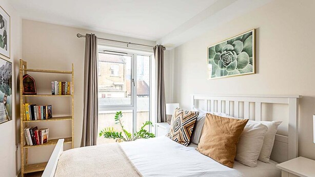 Une chambre bien rangée, avec un lit, des tables de chevet, une bibliothèque et une fenêtre avec des rideaux.