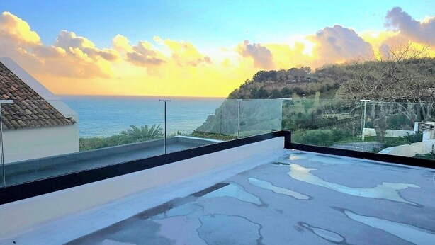 A rooftop terrace with a view of the sea and a hilly landscape.