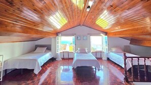 A room with wooden ceiling beams, a central bed, and two smaller beds on either side.