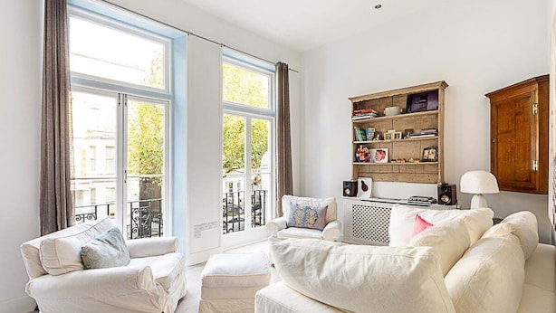 Ein Wohnzimmer mit Sofa, Sessel und Hocker, einem Bücherregal und einer Lampe.