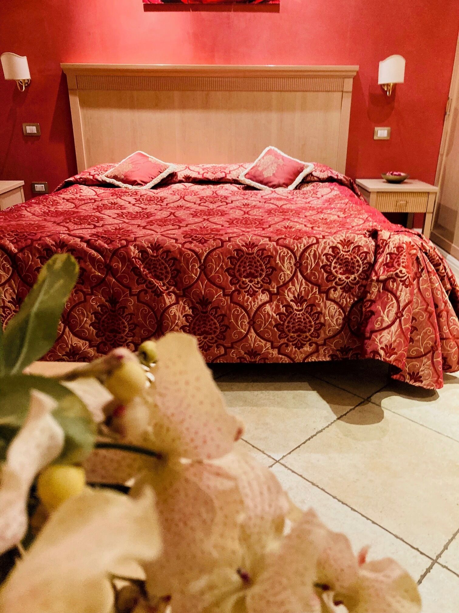 Une chambre d’hôtel avec un grand lit, des murs rouges et une petite table de chevet avec une lampe.