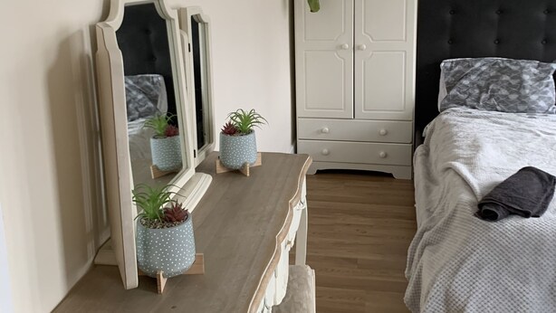 Een slaapkamer met een bed, een nachtkastje met twee planten in potten, een dressoir en een spiegel.