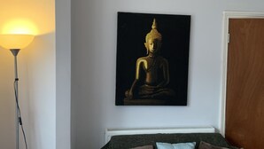 Een kamer met een bed, een boeddhabeeld aan de muur en een staande lamp.