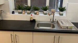 Een keuken met een zwart aanrecht, witte kastjes, een roestvrijstalen spoelbak en potplanten op de vensterbank.