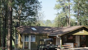 Une cabane rustique avec un garage, un espace extérieur aménagé et couvert, et un véhicule garé devant.