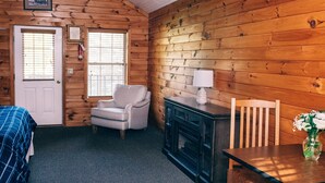 Une chambre confortable dans un chalet, avec un lit, une chaise, une table ornée d’un vase et une cheminée.