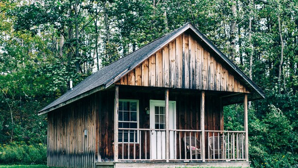 Une cabane en bois rustique, dotée d’un porche et d’une porte, entourée d’une végétation luxuriante.