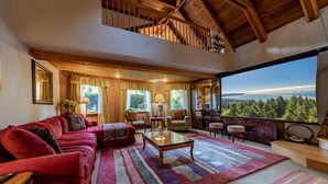 Un salón amplio con un sofá rojo, una mesa de centro de vidrio y vistas a un paisaje boscoso a través de grandes ventanales.