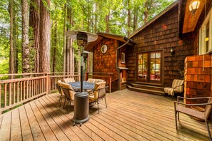 A wooden deck with a table and chairs, surrounded by tall trees.