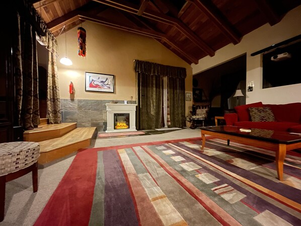 A cozy living room with a fireplace, a red sofa, and a patterned rug.