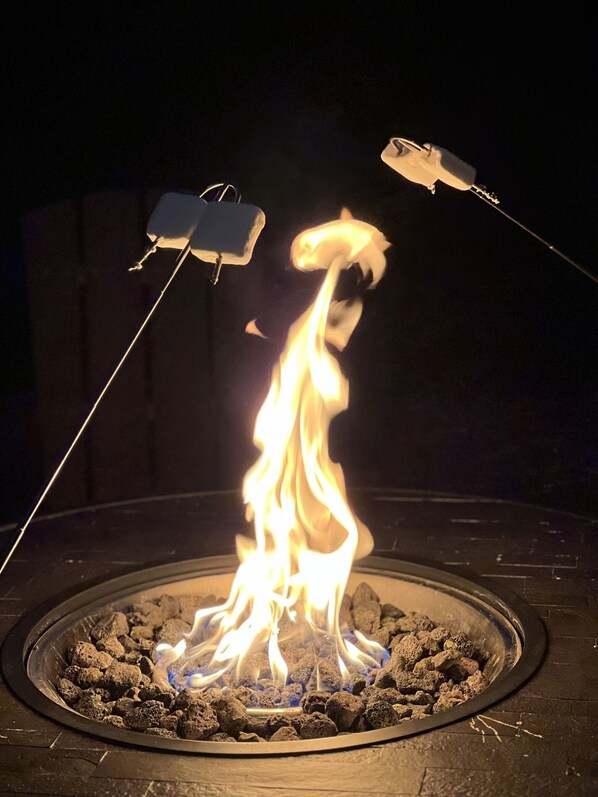 A circular fire pit with a visible flame, surrounded by charcoal.