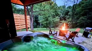 Een hottub met groene verlichting, omringd door buitenmeubels en een vuurkuil.