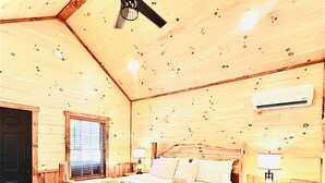 Een slaapkamer in een houten chalet, met een bed, nachtkastje, plafondventilator en airconditioning.