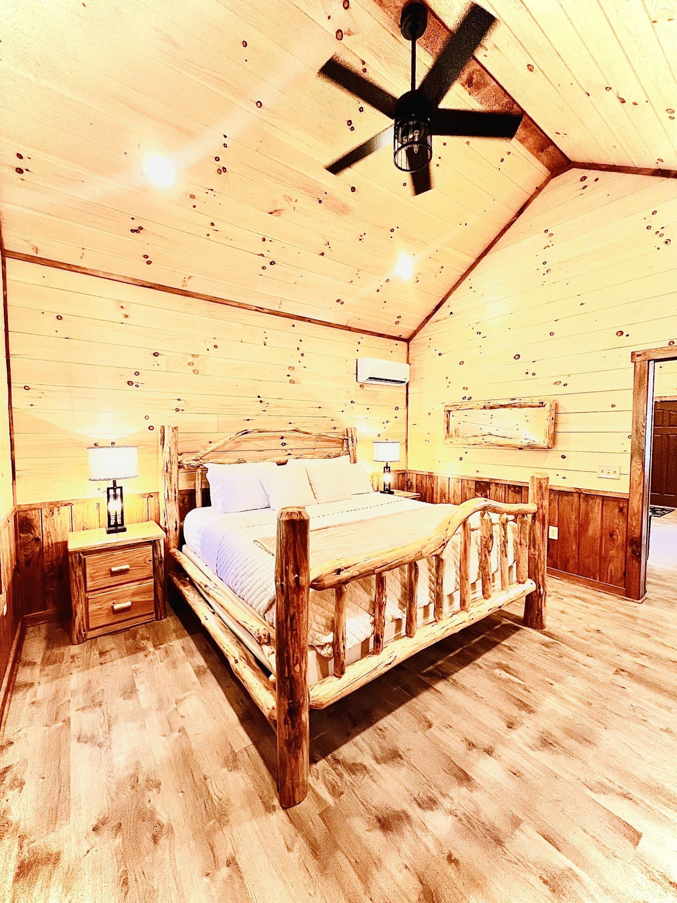 Ein Schlafzimmer aus Holz mit Bett, Nachttischen, Deckenventilator und Klimaanlage.