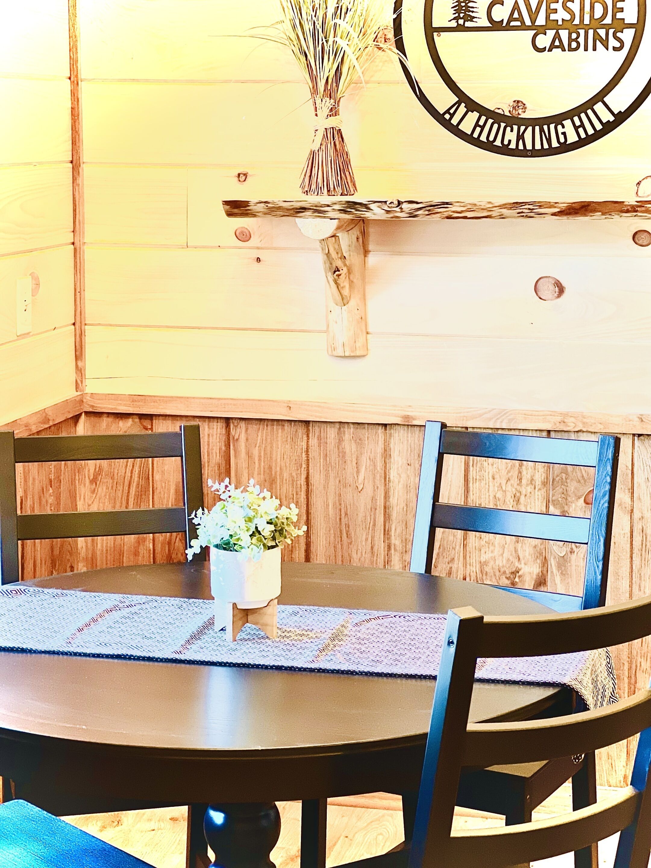 A wooden dining table with chairs, a potted plant, and a sign for 'Caveside Cabins At Hocking Hill'.