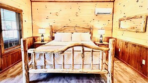 A wooden room with a bed, two bedside tables, a ceiling fan, and a window with blinds. - LUXURY COUPLES CABIN! Caveside Cabins (Creola)