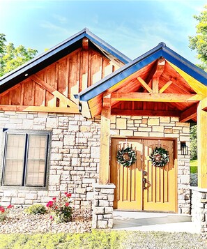 A stone building with a wooden facade, a stone chimney, and a wooden door with two wreaths.