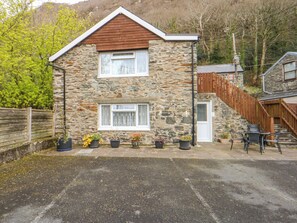 A stone house with a wooden roof, a front door, and a staircase leading to a wooden deck.