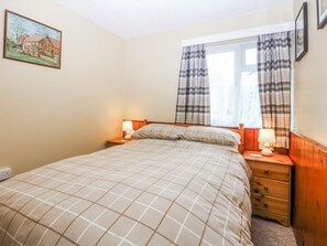 A bedroom with a bed, two bedside tables with lamps, a window with curtains, and a painting on the wall.