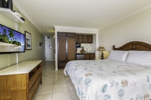A bedroom with a bed, a TV, a wooden dresser, and a kitchen area in the background. - Islander on the Beach 232: Beach Resort Room w/ View, AC & Kitchenette (Kapa'a)