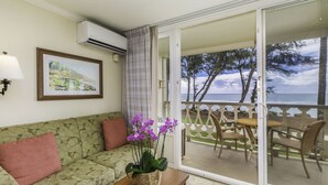 A room with a sofa, a table with a plant, a framed picture on the wall, and a balcony with chairs and a view of the sea. - Islander on the Beach 232: Beach Resort Room w/ View, AC & Kitchenette (Kapa'a)