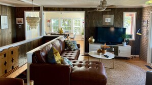 Ett vardagsrum med en brun lädersoffa, en tv och en matplats med ett bord och stolar.