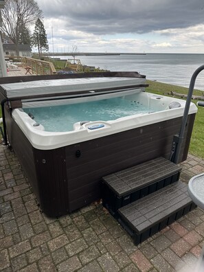 Un jacuzzi con escalones de acceso, ubicado en una zona pavimentada con vistas al agua y un cielo nublado.