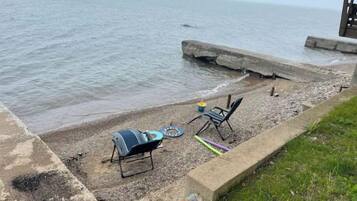 Une terrasse au bord de la plage, équipée d’un barbecue, de chaises et d’une petite table.
