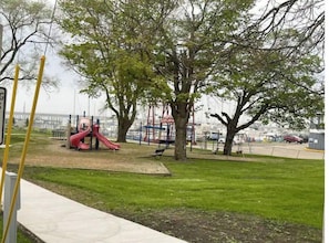 Explore the playground with a slide and swings, surrounded by a shaded walkway and a scenic view.