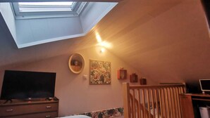 A bedroom with a skylight, a bed, a TV, a desk, and a staircase. - Studio close to ocean and shops (Givrand)