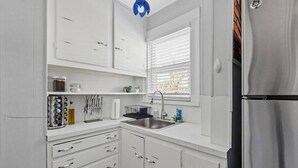 A compact kitchen with white cabinets, a stainless steel sink, and a refrigerator. - Cozy House close to TUFTS, Harvard, MIT 3BR (Medford)