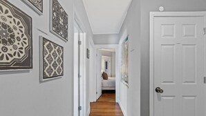 A hallway with patterned wall decorations, a wooden floor, and a white door. - Cozy House close to TUFTS, Harvard, MIT 3BR (Medford)