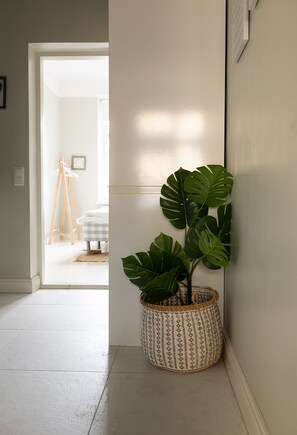 A hallway with a potted monstera plant, a wooden easel, and a framed picture on the wall. - 2ndhomes Modern 1BR Home in Ullanlinna (Helsinki)