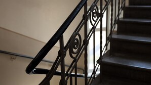 Eine Treppe mit aufwendiger, schwarzer Metallreling und einer beige gefärbten Wand.