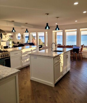Una cocina moderna con una isla central, armarios blancos y vistas al mar a través de amplios ventanales.