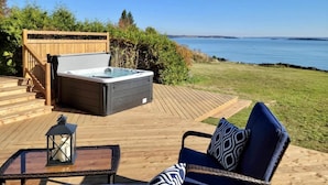 En terrasse med jacuzzi, udendørs møbler og havudsigt.