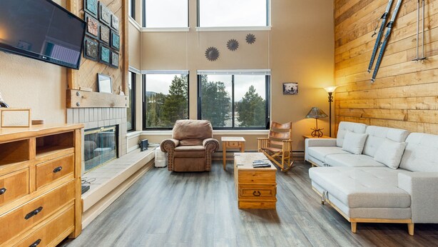 A spacious living room with a large window, a fireplace, a sofa, a chair, and a TV mounted on the wall. - Spacious Condo/Mountain Views/Great Amenities (Keystone)