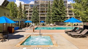 A swimming pool area with lounge chairs and umbrellas, surrounded by a multi-story building with balconies. - Spacious Condo/Mountain Views/Great Amenities (Keystone)